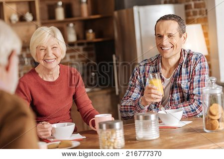 Mood-boosting conversation. Pleasant upbeat family sitting at the kitchen counter, having breakfast and talking to each other while exchanging smiles