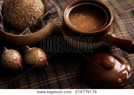 Food, a soup broth  and seeded Roll winter warming lunch, showing a rustic food scene with wooden bread dish and earthenware crockery soup dish with lid.