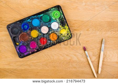 Box with watercolors and brushes on wooden surface. Top view