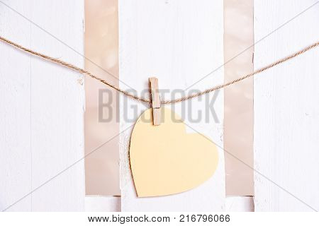 Yellow heart with wooden clip on string - Paper note heart-shaped tied to a linen string with a wooden clip on a white wooden fence background. A concept of love communication greeting card.