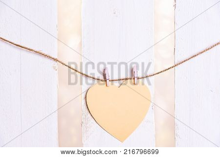 Heart shaped message card on a string - Romantic image with a yellow heart-shaped paper note tied to a string with two wooden clips on a white wooden fence background.