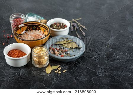 Pink, gold and white salt, black and red peppercorns, bay leaf, paprika on a black background Top view.