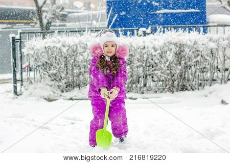 Little girl with green showel cleaning roads at winter morning