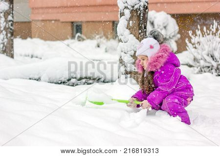 Little girl with green showel cleaning roads at winter morning