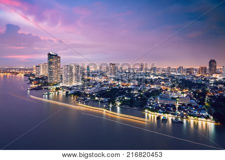 Bangkok during dusk. City skyline with traffic (boats in blurred motion) on the Chao Phraya River.