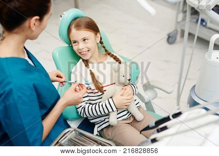 Happy little patient with teddybear listening to dentist advice about brushing teeth in clinics