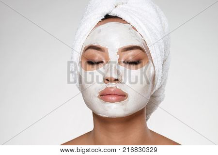 Portrait of beautiful lady with closed eyes and towel on her head put scrab on her face isolated