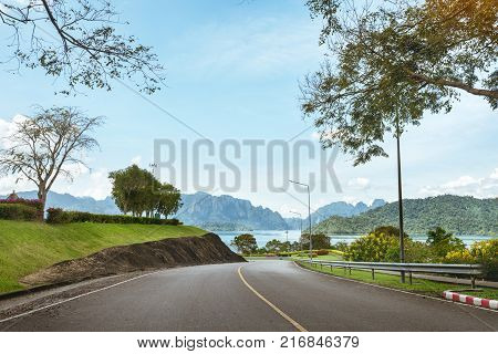 Beautiful tropical landscape with straight road, lake and mountains on background. Cheowlan lake, Khao Sok national park, Rachaprabha dam, Suratthani province, Thailand