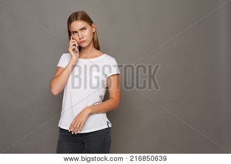 Concentrated young woman talking on mobile portrait on gray stusio background. Family issues, problem concept