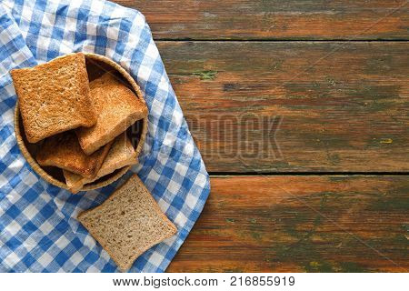 Breakfast background, white bread toasts in wicker breadbasket on checkered table napkin half covering wooden table, top view, copy space