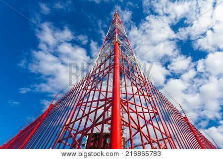 Telecommunication tower with panel antennas and radio antennas and satellite dishes for mobile communications (2G 3G 4G 5G) with red fence around tower against blue with clouds