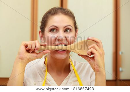Cooking and preparing food meal concept. Thoughtful wondering and confused woman chef cook housewife holding biting ladle spoon in kitchen.