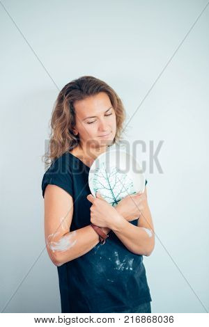 potter, tools, ceramics art concept - handsome young brunette female stand with finished utensils, smiling ceramist at workplace with baked cups and jugs at background