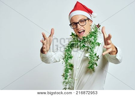 man with green tinsel on his neck smiling and pulling his hands forward, bright background, christmas, new year.