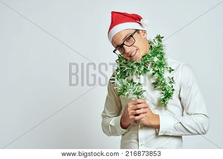 man with green tinsel smiling, light blue background, free space for copy.