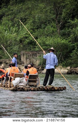 September 6 2016. Wuyishan China. Boatmen using bamboo sticks to steer the bamboo boats down the Jiuqu Xi river or nine bend river in Mount Wuyi Scenic area in Fujian province China on an overcast day.