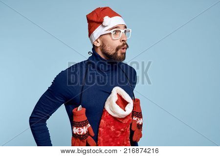 bearded man with a Christmas sock on his chest looks surprised at free space to copy, light blue background.