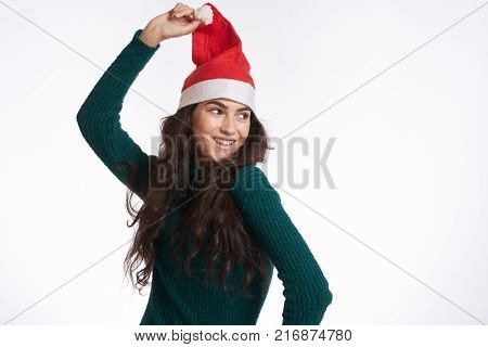 woman in green dress holds herself for a Christmas hat and smiles, light background, winter.