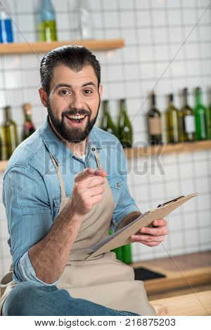 Bright idea. Positive emotional bearded man looking excited while sitting and smiling with his finger pointing in front of himself