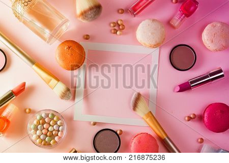 Make up products and macaroons frame with copy space on pink background, toned