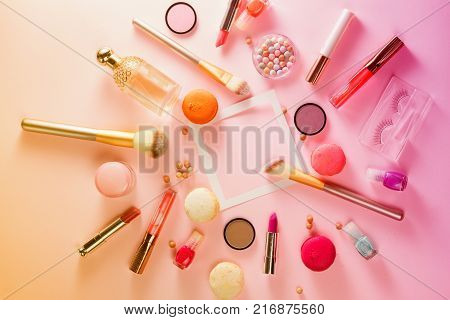 Make up products and macaroons flat lay frame with copy space on pink background, toned