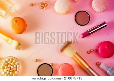 Make up products and macaroons flat lay scene on pink background, toned