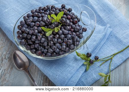 Fresh forest berry, blueberries in a glass plate on a wooden table.