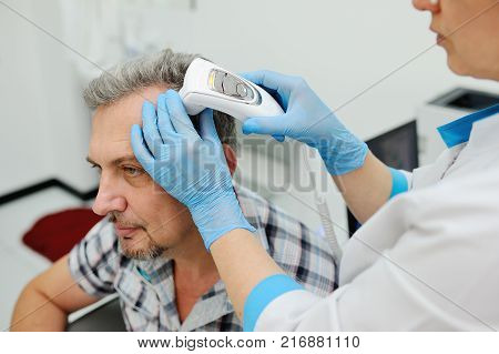 baldness. doctor examines an elderly man hair using special equipment - trihoskopa
