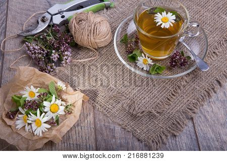 Cup of tea with chamomile ang origano flowers on rustic wooden background.