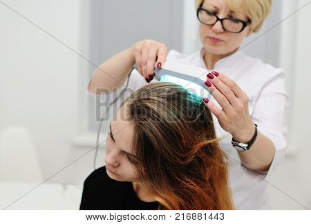 Doctor examines scalp a pretty young girl with special instrument UV lamp. Skin problems, dermatology, shingles, psoriasis, redness, prevention