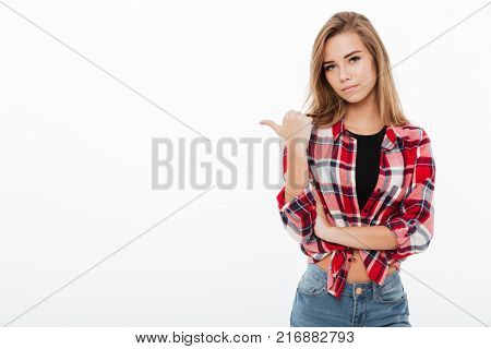 Portrait of a lovely pretty girl in plaid shirt standing and pointing finger away at copy space isolated over white background