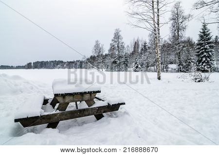 Wooden bench and table covered of snow in a snowy forest landscape. Winter picnic