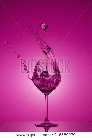 Water splash in out of glass. Water splashing out of a tall wine glass. purple gradient background. Reflection.