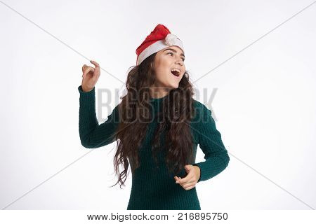 woman in Christmas hat gestures and smiles, light background, new year, christmas, winter.