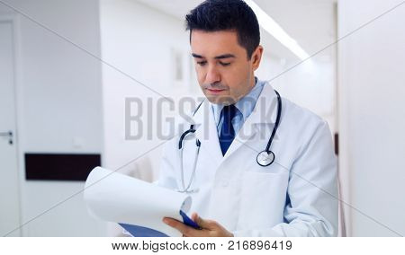 medicine, healthcare and people concept - doctor writing to clipboard at hospital
