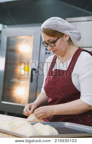 Adult woman in glasses and apron bakes cakes in the bakery half-profile smiling close-up