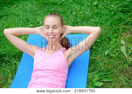 Beautiful sport woman doing stretching fitness exercise in city park at green grass.