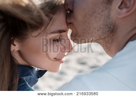Beautiful couple, man and girl kissing and hugging on a sandy beach by the sea at sunset in sun glasses
