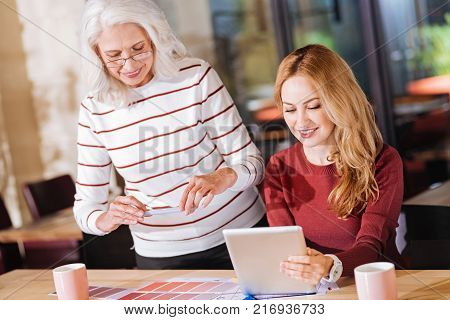 Great colors. Progressive enthusiastic senior woman taking photos of a color palette while a young cheerful designer looking at the screen of a tablet