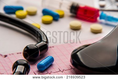 plastic syringe pills and stethoscope on cardiogram