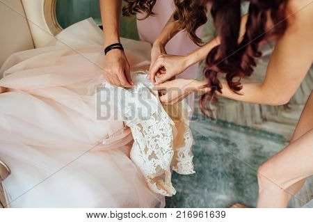 Bridesmaid preparing bride for the wedding day, helping fasten her dress