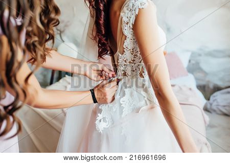 Bridesmaid preparing bride for the wedding day, helping fasten her dress