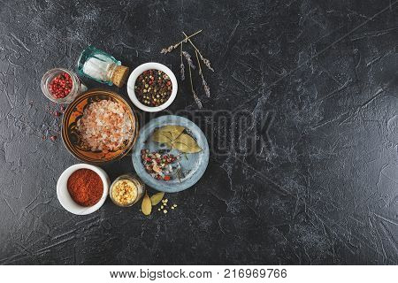 Pink, gold and white salt, black and red peppercorns, bay leaf, paprika on a black background Top view.