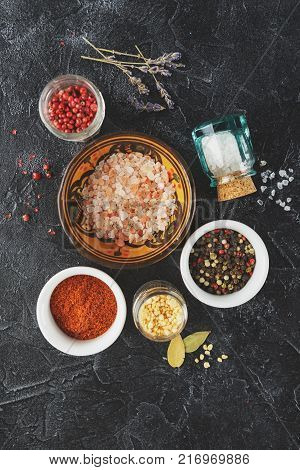 Pink, gold and white salt, black and red peppercorns, bay leaf, paprika on a black background Top view.