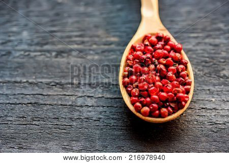 Close up wooden spoon with pink peppercorn on dark background