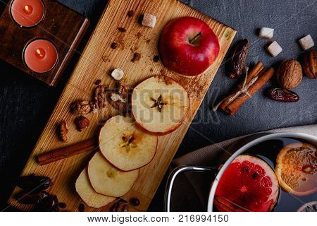 A chopped apple with dates, nuts on a wooden dinette, a burning candle, cinnamon, sugar cubes and a sangria pan. View from above