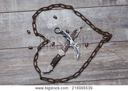 The chain is rusty in the form of a heart with knives inside and scattered bullets on a wooden background