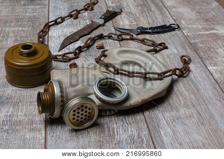 A gas mask disassembled with a rusty chain with knives folding and self-made on a wooden floor. View at an angle