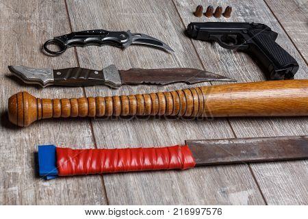A bandit chain gun, a machete, a bat, knives and a bullet with bullets lie horizontally in a row on a wooden floor. View at an angle