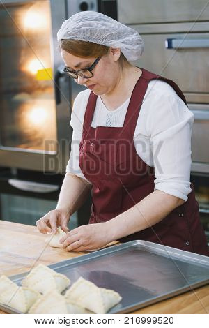 Adult woman in glasses and apron bakes cakes in the bakery half-profile close-up